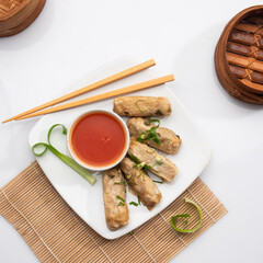 A plate of crispy spring rolls sits clear of distractions, accompanied by a small bowl of tangy dipping sauce and chopsticks by the side