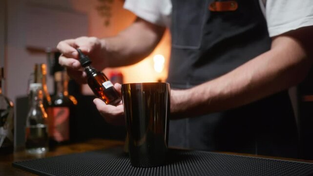 Bartender dripping bitters into a shaker. Crafting a cocktail at home.