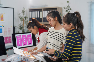 Three asian female ux designers collaborating on mobile app wireframes and prototypes in a modern...