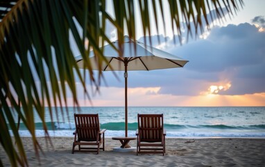 Obraz premium A tranquil beach scene at sunrise with two wooden lounge chairs positioned under a white umbrella.