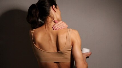 Strong sporty fit woman take care of her shoulder and neck skin. Touching and massaging muscules holding the container with ointment, tube cream. Skin body care. Closeup beauty video