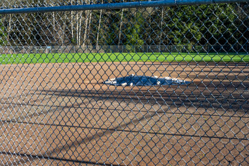 Looking through a chain link fence at a baseball diamond with the pitcher&rsquo;s mound covered and protected for winter by a black tarp secured by white weights, sports and recreation background
