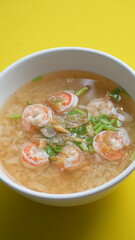 rice soup with shrimp in white bowl on yellow background