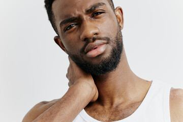 African american man in white tank top holding neck, showing discomfort or pain in an indoor setting
