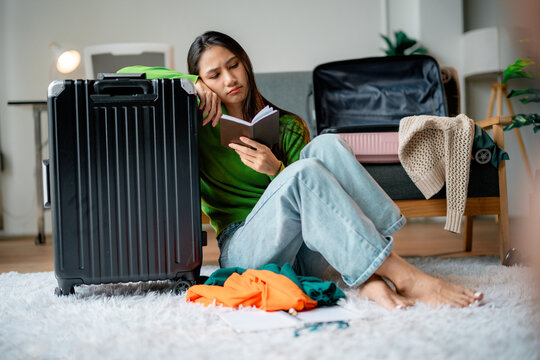 Stressed young woman holding passport feeling sad while packing clothes for travel trip at home