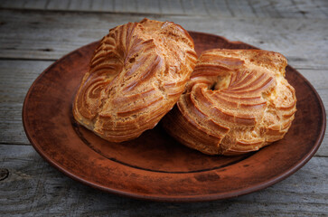 A clay plate with profiteroles stands on a wooden surface. Profiterole cake. Eclair in the form of...