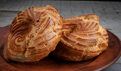 A clay plate with profiteroles stands on a wooden surface. Profiterole cake. Eclair in the form of a ring.