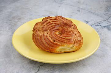 The profiterole cake is on a yellow plate. The eclair is in the shape of a ring.