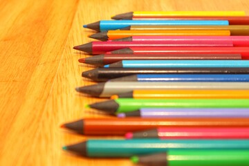 Colorful pencils lined up isolated on a wooden background, close up view.