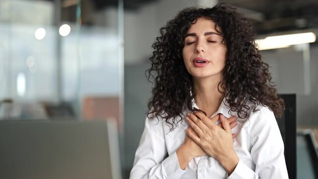 Curly-haired businesswoman in office suffering from sudden chest pain, shortness of breath, panic attack, heart attack, or hot flash.