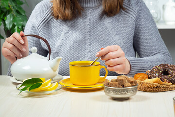 Woman in a sweater, holding a cup of hot tea. Hands close-up.