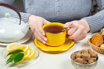 Woman in a sweater, holding a cup of hot tea. Hands close-up.