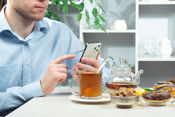 A young man in a blue shirt holds a cup of tea in his hands. He adds sugar to taste and stirs it. Close-up of his hands.