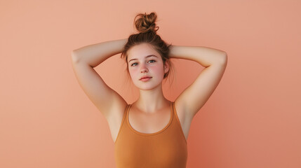 Obraz premium Simple Serenity: A young woman exudes tranquility, her hands gently resting on her head as she gazes into the camera, radiating a sense of peace and self-assurance. Her natural beauty shines through.