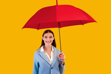 Portrait of cheerful pretty lady standing under yellow umbrella at pink studio, looking at camera