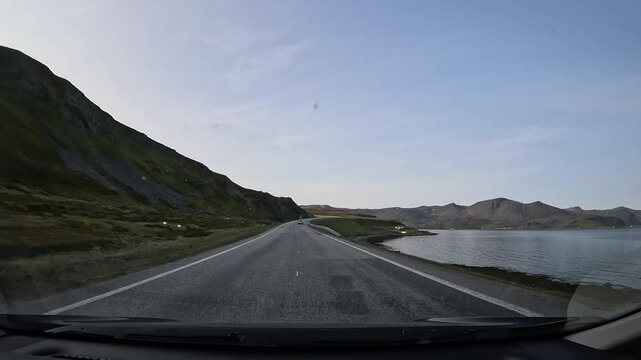 Driving through the tundra landscape of northern Norway on the E69 road. Rocky hills with grass surround the road. The sea is visible on the right side.