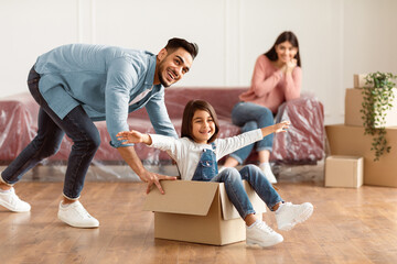 At New Apartment. Happy loving family having fun and celebrating moving day, excited man riding...