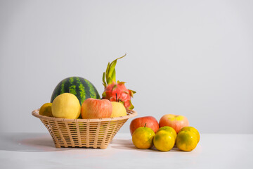 A basket filled with mixed fruits, including apples, placed on a table against a white background, offering a fresh, vibrant display of healthy, natural produce perfect for any setting