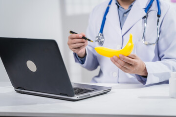 A male nutritionist working at a hospital desk, holding an apple and mixed fruit, offering care,...
