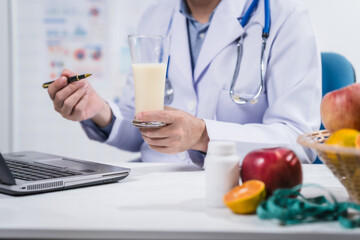 A male nutritionist working at a hospital desk, holding an apple and mixed fruit, offering care, health advice, weight loss guidance, and eating tips online for patients seeking nutrition support