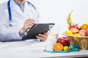 A male nutritionist working at a hospital desk, holding an apple and mixed fruit, offering care, health advice, weight loss guidance, and eating tips online for patients seeking nutrition support