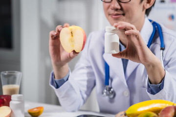 A male nutritionist working at a hospital desk, holding an apple and mixed fruit, offering care, health advice, weight loss guidance, and eating tips online for patients seeking nutrition support