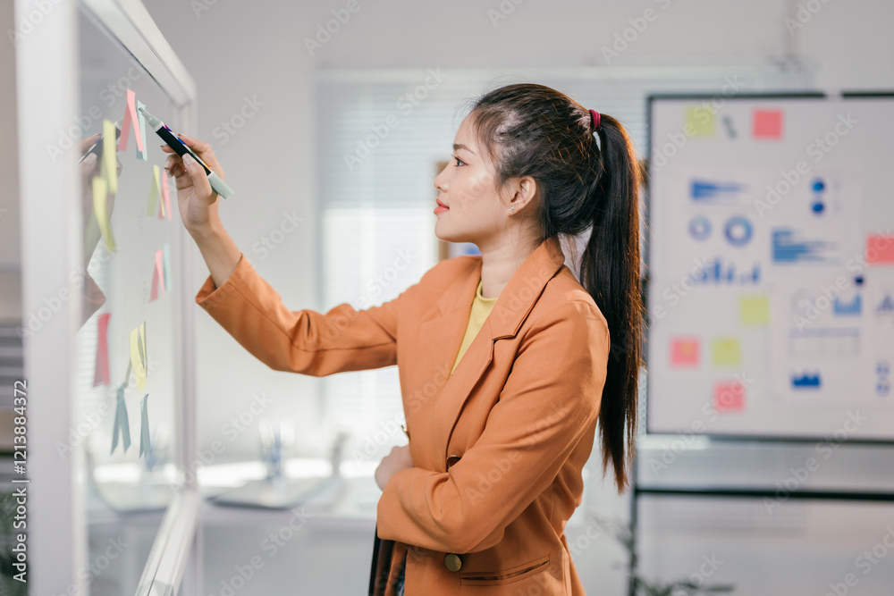 Poster Businesswoman using colorful sticky notes while brainstorming and strategizing on a transparent whiteboard in a modern office