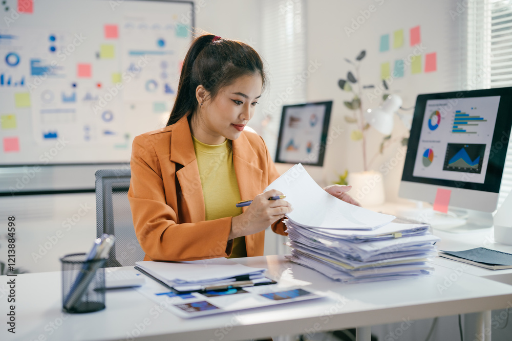 Aufkleber asian businesswoman reviewing paperwork and using computer with data analysis displayed on screen