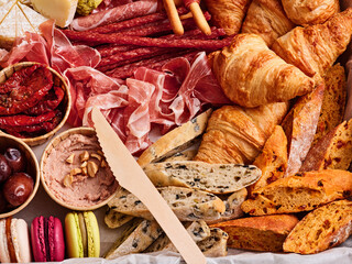 A vibrant display of charcuterie features a variety of cured meats, fresh croissants, gourmet cheeses, and colorful macarons, perfect for a festive gathering or casual dining