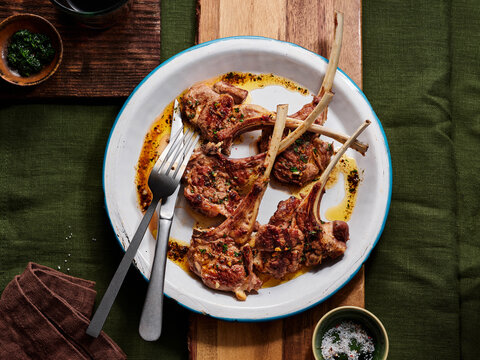 Tender lamb chops are beautifully arranged on a white plate, showcasing a golden-brown crust and topped with fresh herbs. The rustic wooden table enhances the inviting atmosphere