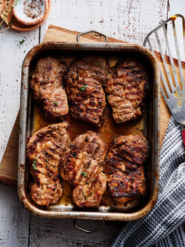 Delicious, expertly grilled steaks rest in a metal tray, garnished with fresh herbs. The rustic wooden table and kitchen utensils create a warm, inviting atmosphere