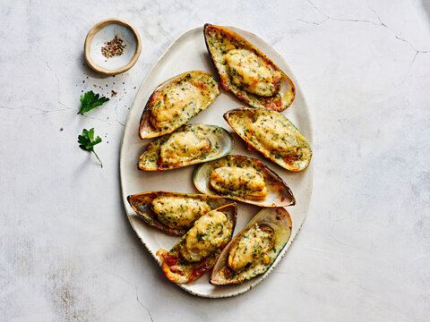 A platter of baked mussels is perfectly arranged, showcasing a golden, cheesy topping sprinkled with fresh herbs. This dish highlights Mediterranean flavors and is ideal for sharing