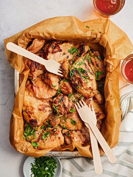 Juicy grilled chicken pieces are arranged on a tray lined with parchment paper. Fresh herbs are sprinkled on top, complemented by two drinks nearby, creating an inviting atmosphere