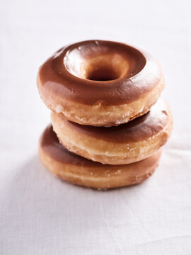 Three delicious glazed donuts sit atop each other on a clean white surface. Their shiny brown coating glistens, making them an inviting choice for breakfast or dessert