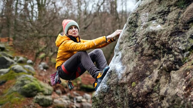 A woman engaged in bouldering on a rocky surface, dressed warmly for the cool outdoors. The image captures the spirit of adventure, strength, and outdoor activity.