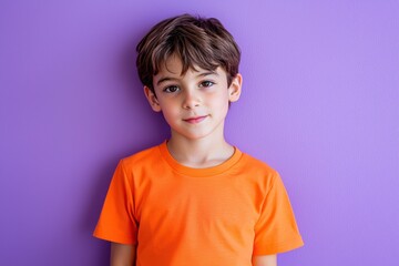 Cute boy in an orange shirt, standing on purple background.