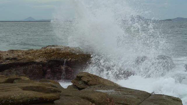 Ocean waves crash against the rugged rocky shore at Point Cartwright, unleashing a powerful splash of seawater that soars high into the air.