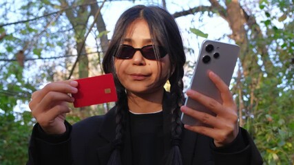 A woman in the park completes an online purchase using her smartphone and credit card, enjoying the convenience of digital banking.