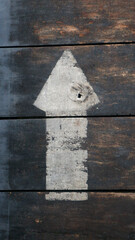 The white arrow sign on the old wooden board is too worn out from use.