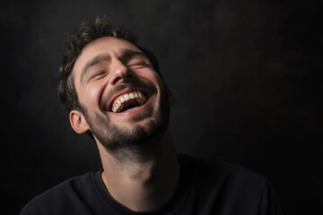 Fototapeta premium Portrait of a cheerful young man laughing with closed eyes and head tilted back, expressing happiness and joy on a dark background