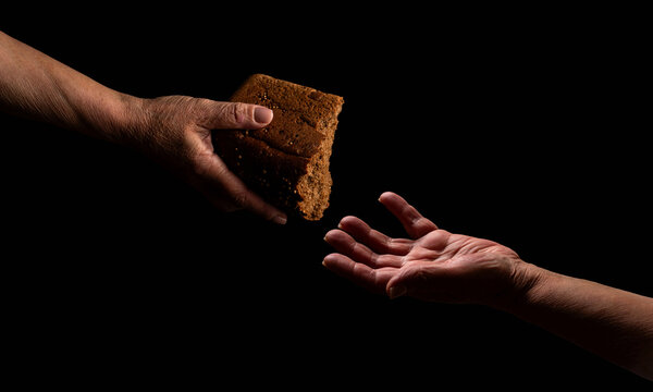 Elder woman hand give a loaf of bread to hands of a beggar. Poverty and world hunger concept. Hands grabbing for bread. Old man giving poor homeless person pieces of bread. Helping the homeless