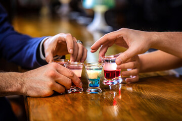 Several alcohol shot glasses.Shots on a bar counter top. Set of shot cocktails. Male hands cheer with glasses of vodka and liqueur. Best friends toasting with cocktails. People drinking at aperitif