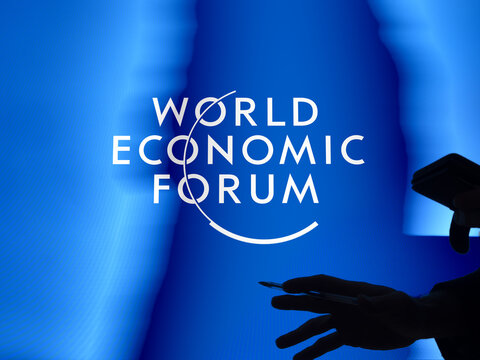 Davos World Economic Forum logo on a window. Passer-by silhouette in the foreground