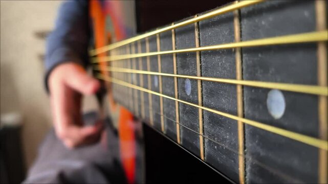 Guitar strings in close-up, a hand playing the guitar in the background, a place for text on the side. Guitar lesson. A musical stringed instrument.