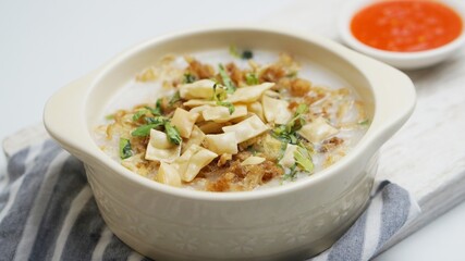 Close up Bubur Ayam, Indonesian rice porridge served with shredded chicken and wonton crackers isolated white background