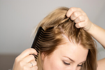 Fototapeta premium Close up portrait of a woman brushing her blonde hair with a black comb 