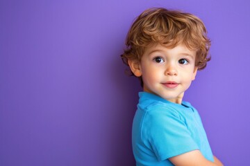 Naklejka premium Little boy in a blue shirt, posing on purple background.