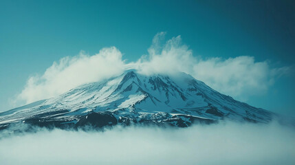 Majestic snow-capped mountain peak shrouded in clouds under a clear blue sky.