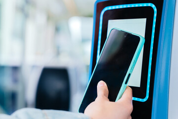 Close-up of a hand using a smartphone to scan a contactless ticket validator on public transport. The digital payment system enables quick and convenient access for commuters in a modern urban setting