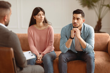 Obraz premium Family Psychologist Concept. Portrait Of Upset Sad Middle Eastern Couple Sitting On Couch Sofa In Office, Discussing Relationship Problems Thinking About Breakup Or Divorce. Mental Health